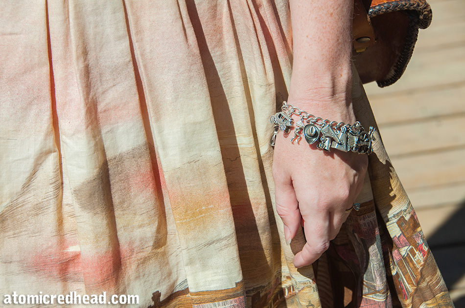 A close up of my charm bracelet, which features an array of vintage western themed charms, including a cowboy hat, gun holster, stagecoach, and tipi.