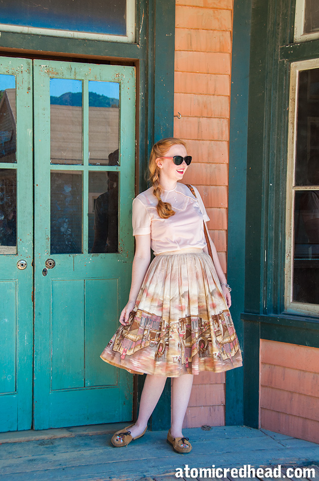 Standing in my outfit I themed for the day, a vintage pale pink nylon blouse, with a vintage border print skirt featuring an illustration of a western town.