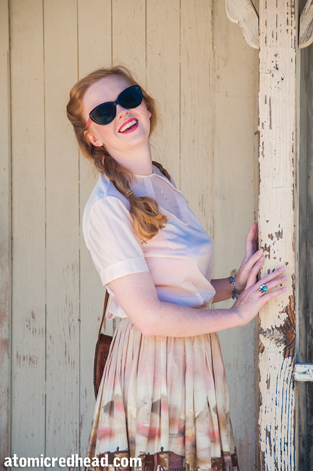 Standing in my outfit I themed for the day, a vintage pale pink nylon blouse, with a vintage border print skirt featuring an illustration of a western town.