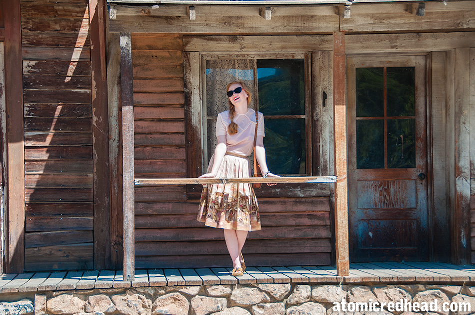 Standing in my outfit I themed for the day, a vintage pale pink nylon blouse, with a vintage border print skirt featuring an illustration of a western town.