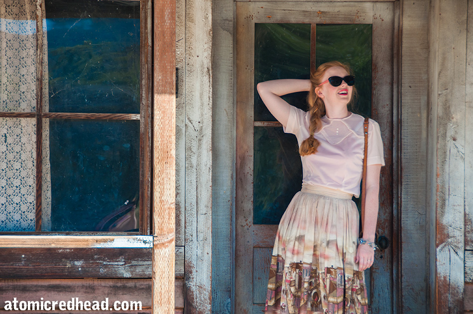 Standing in my outfit I themed for the day, a vintage pale pink nylon blouse, with a vintage border print skirt featuring an illustration of a western town.
