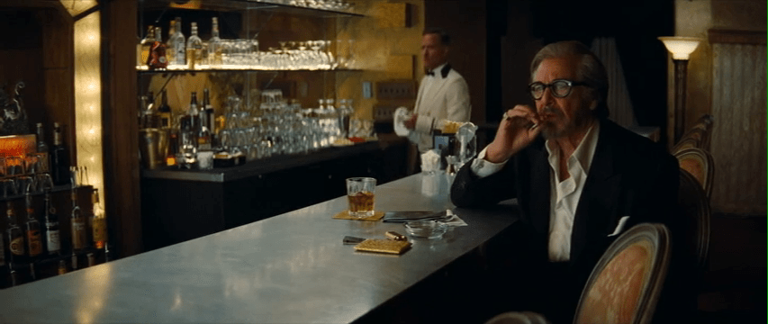 Al Pacino sits at a bar, smoking a cigarette.