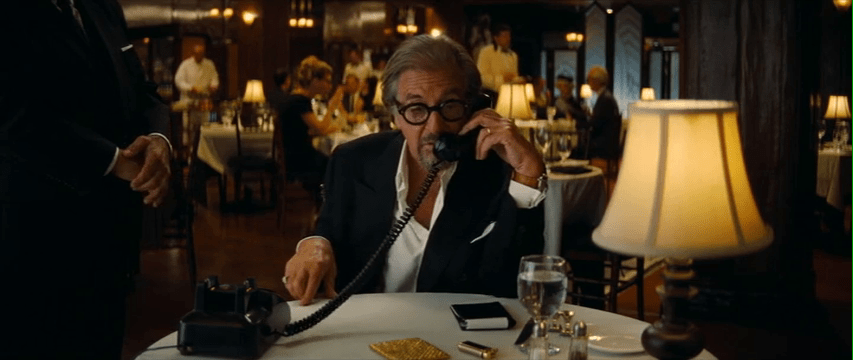 Al Pacino sits at a dining table, talking on a phone.