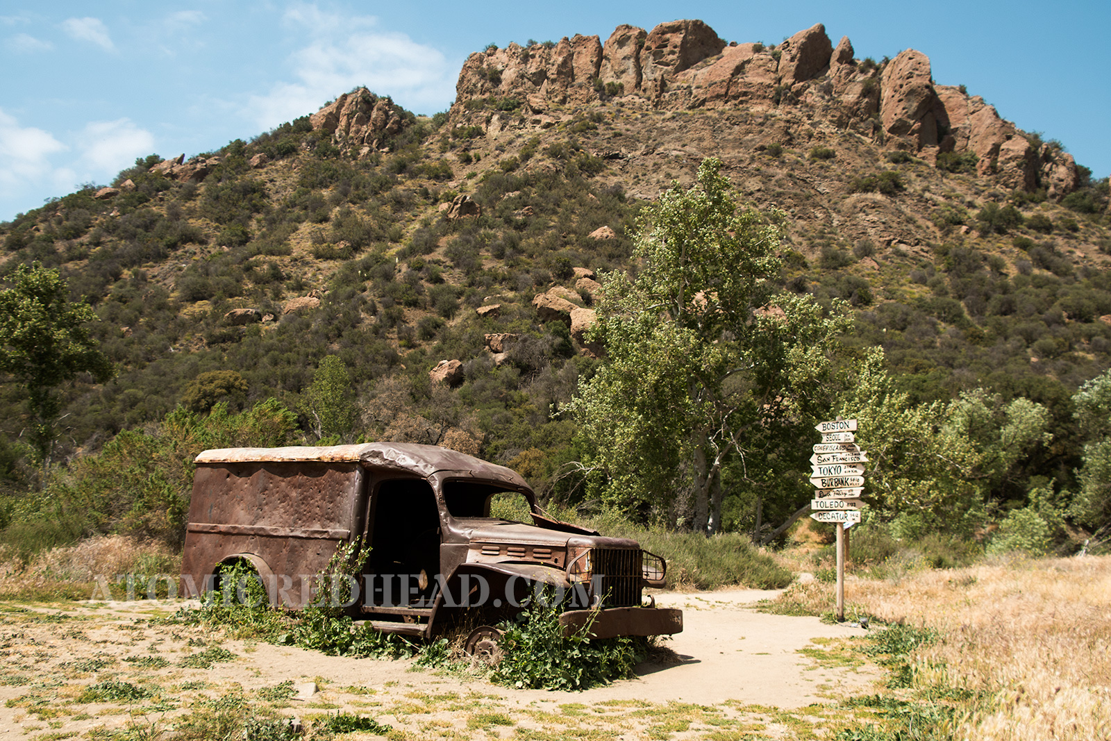 The rusted ambulance in front of the sign post.
