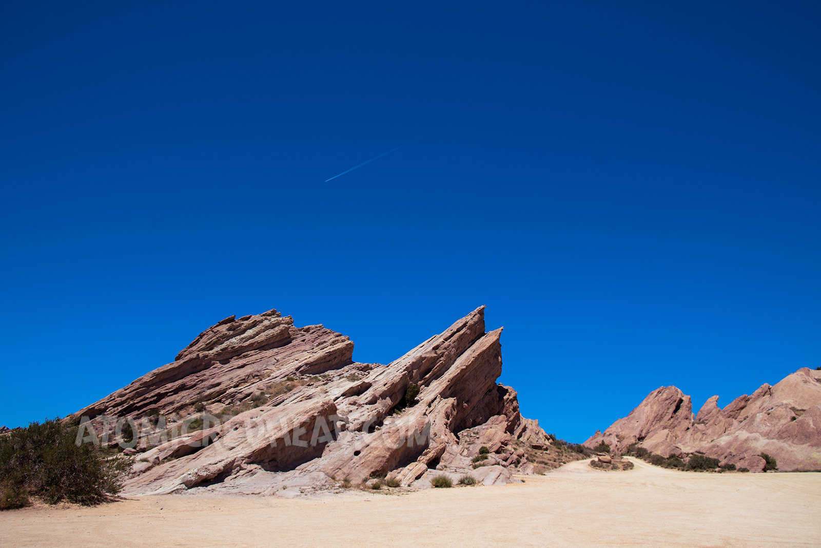 Peaks of Vasquez Rocks with a valley to drive between, against a bright blue sky.