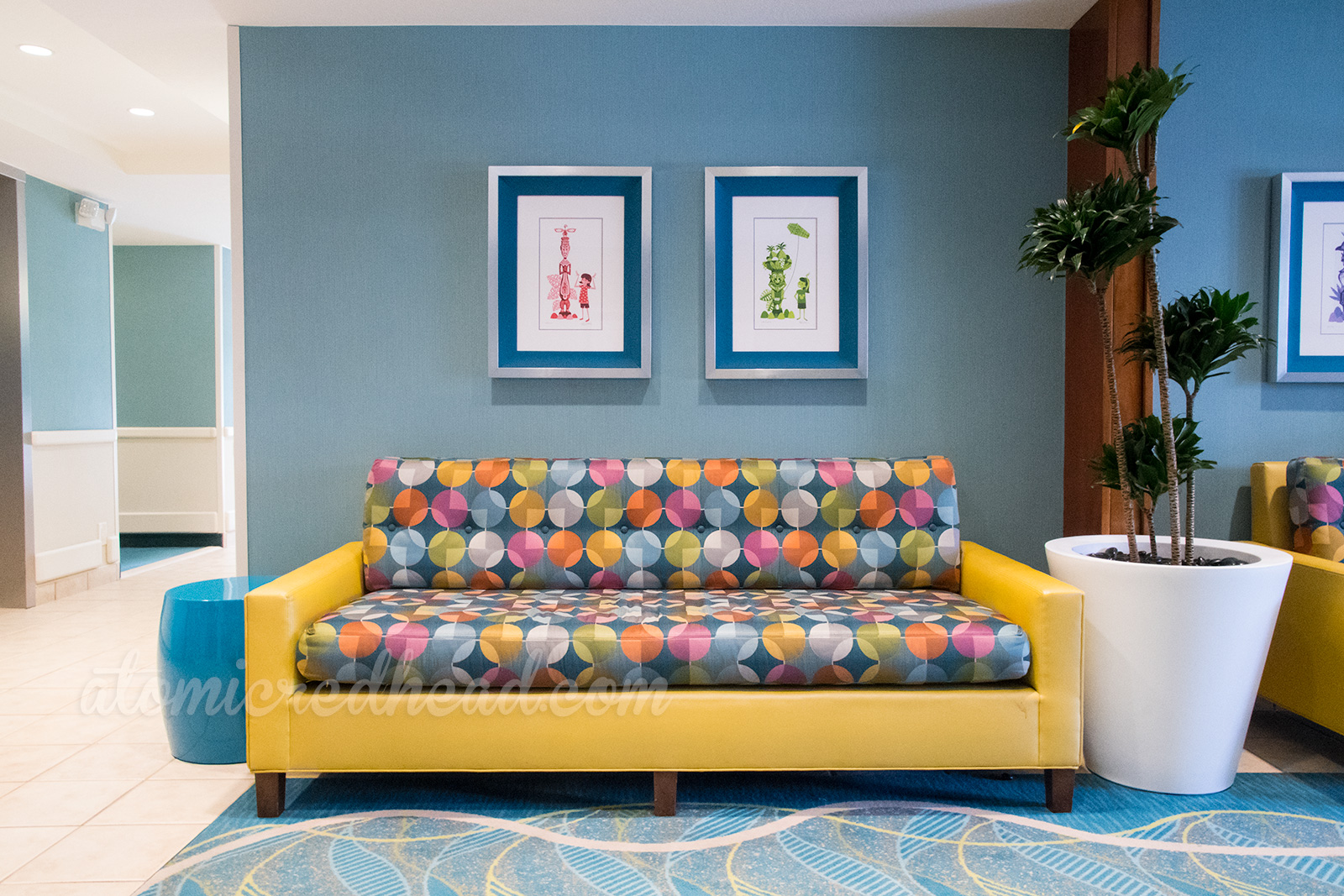 The hallway lobby of one of the towers, featuring geometric patterned carpet, blue walls, and a yellow and multi-colored geometric patterned couch.