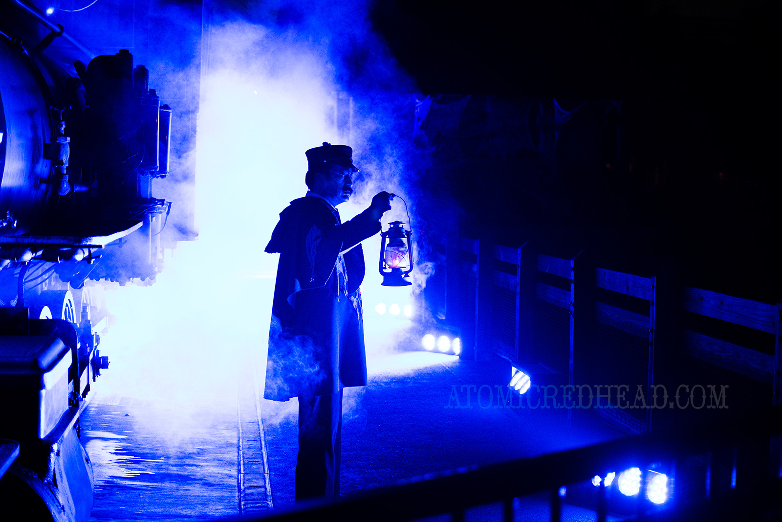 A ghostly train conductor holds a lantern guiding potential passengers through the fog