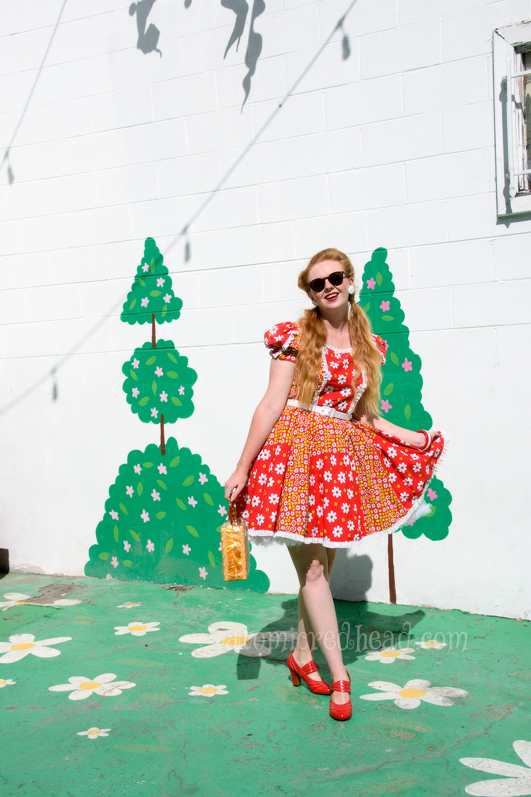 Standing outside the theater, wearing a red square dancing dress with yellow and white flowers.