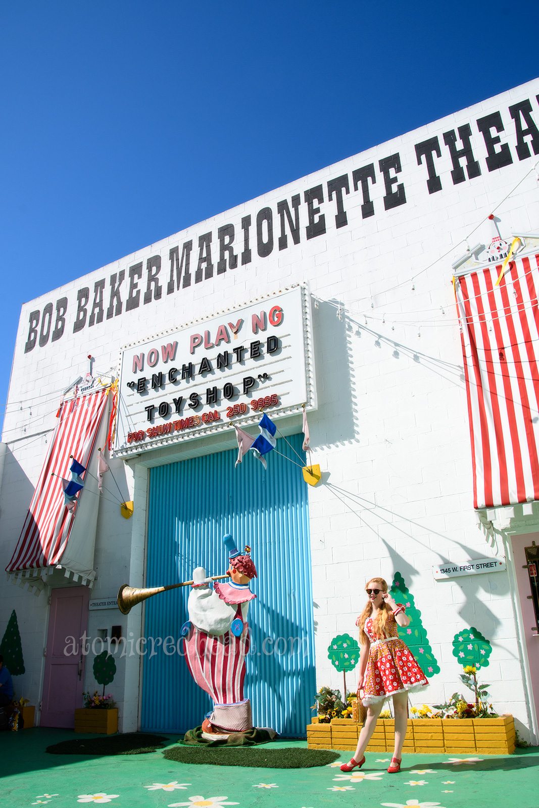 Standing outside the theater, wearing a red square dancing dress with yellow and white flowers.