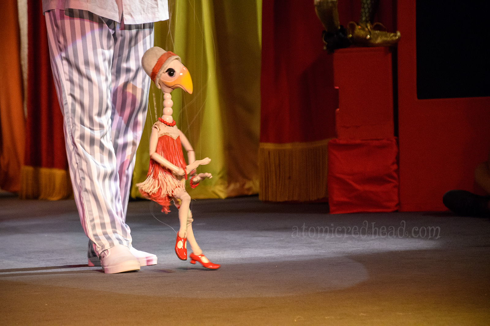 A fanciful goose marionette dressed like a flapper in a ride and white fringe outfit.