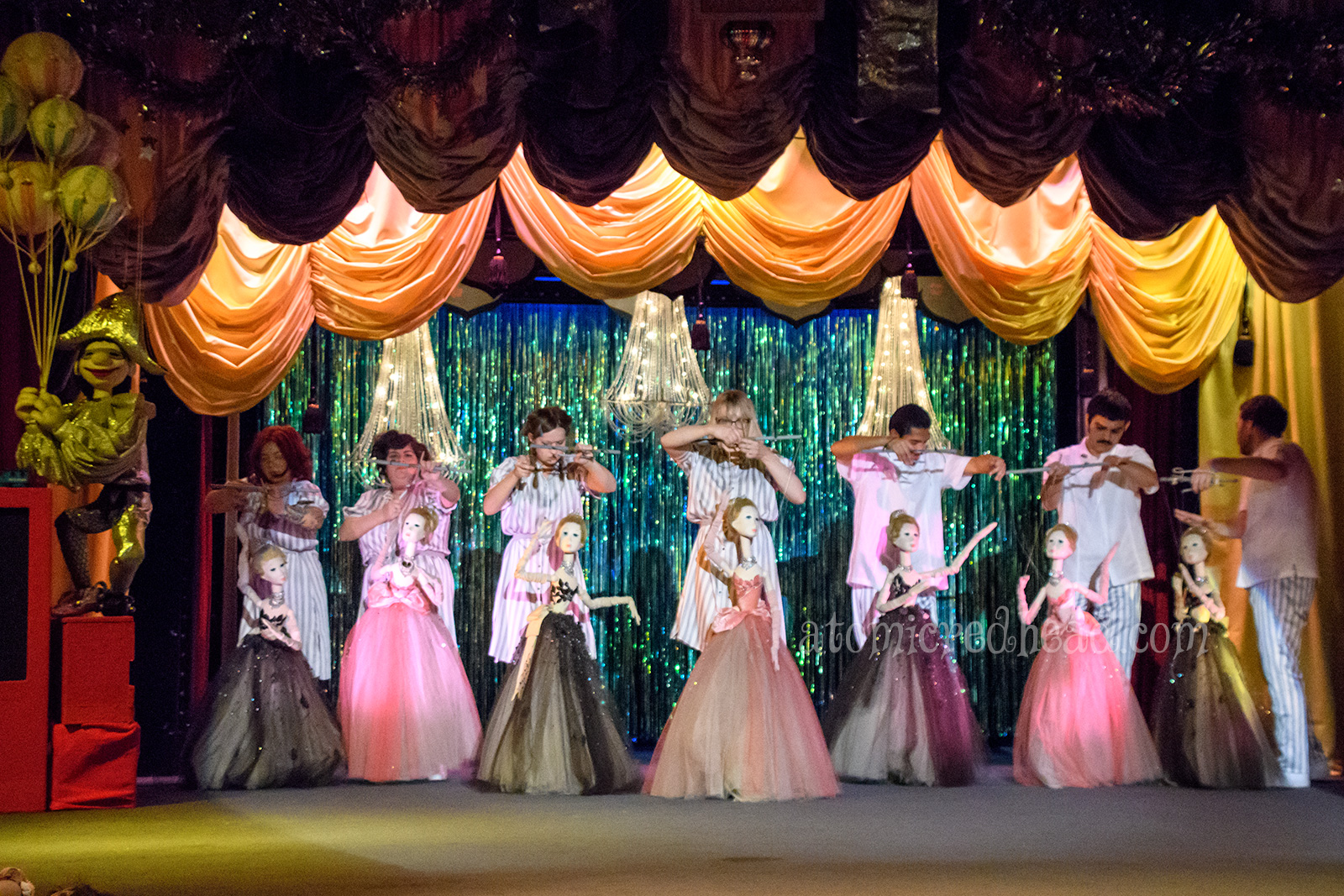 Large marionettes of women wearing tulle prom dresses. Some in black, others in pink.