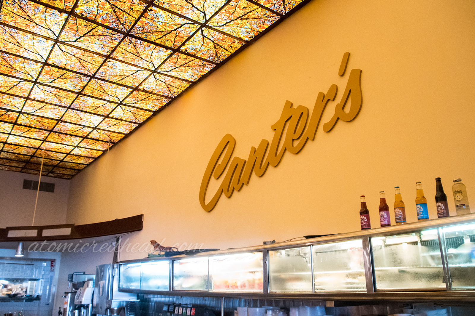 Inside Canter's - large cream walls with tan text reading "Canter's" and a faux stained glass ceiling features an autumn leaf pattern.