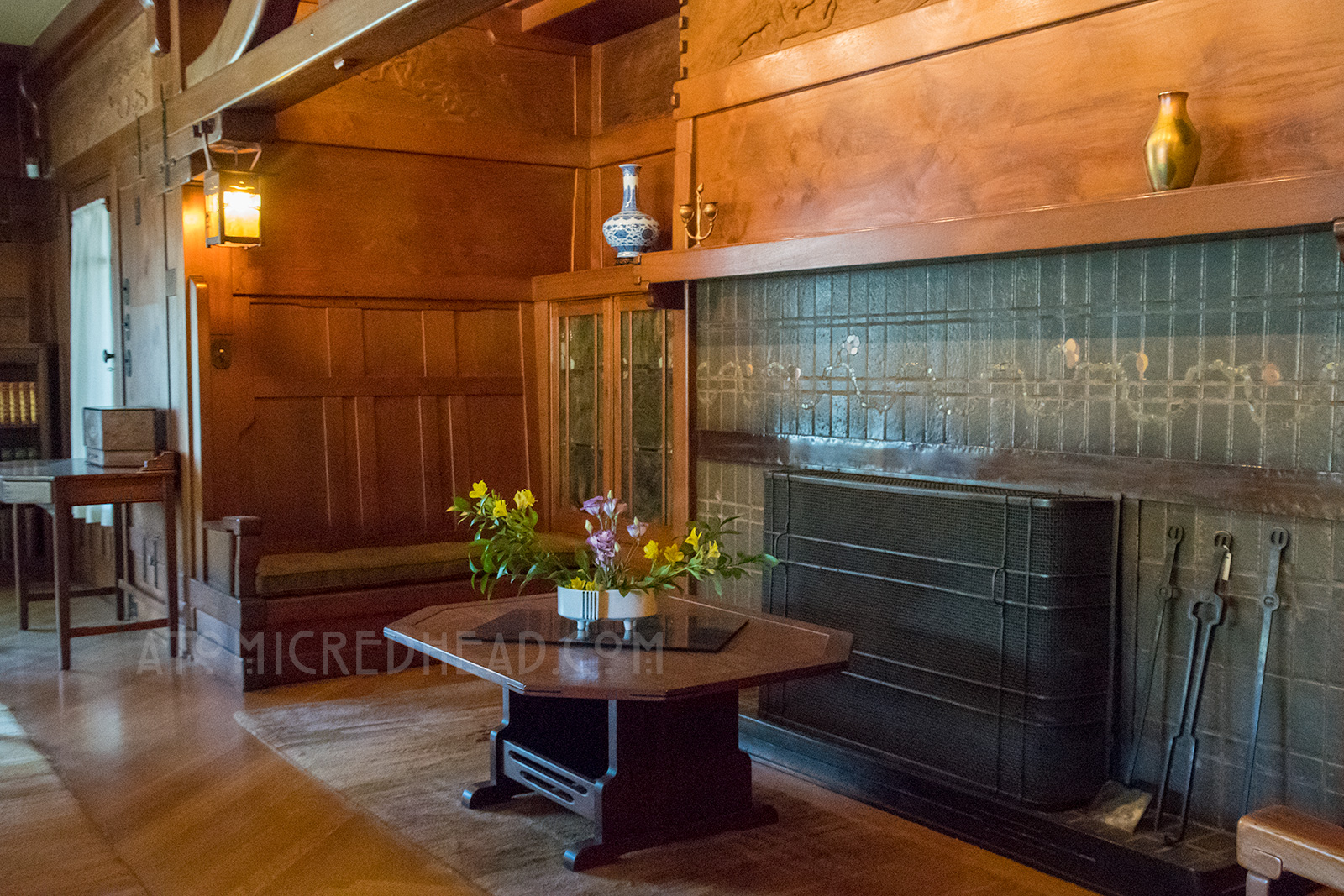 The fireplace of the living room, all rich warm wood, with a dusty green tile fireplace.