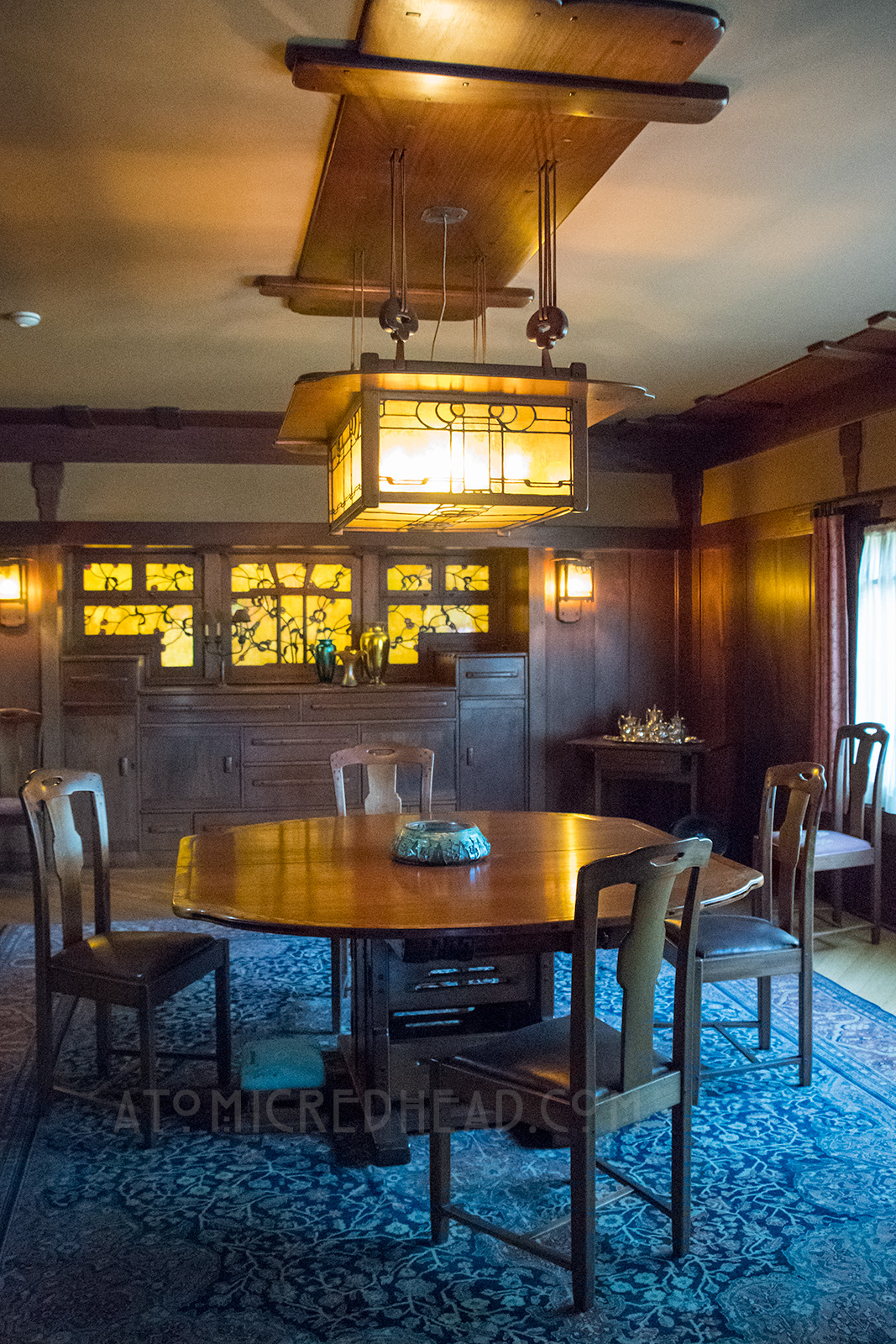 The dining room, dark wood walls, with stained glass of leaves in the back.