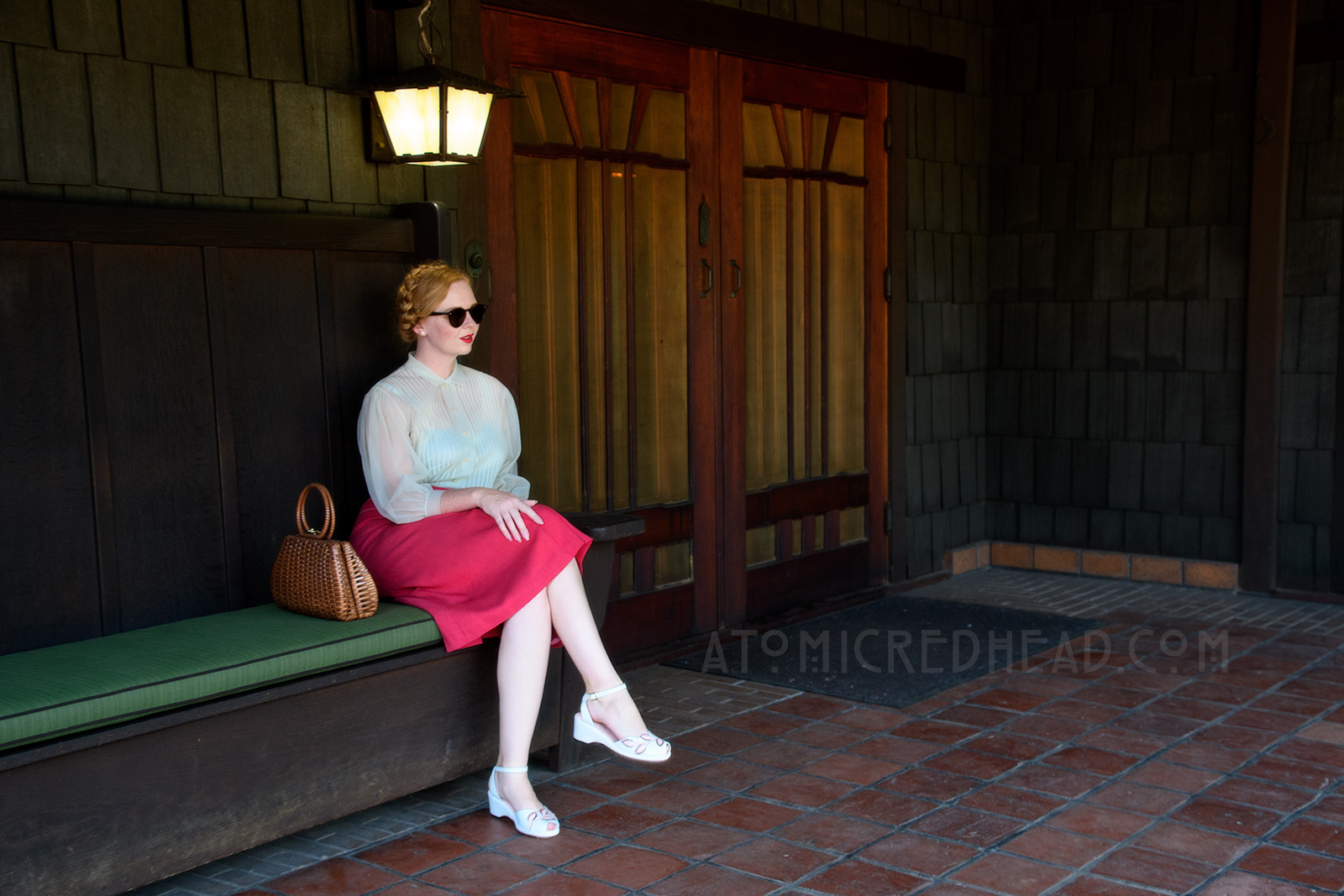 Sitting on the back porch of the Gamble House, wearing a pale blue sheer blouse and magenta skirt with white trim, and a brown woven basket purse.