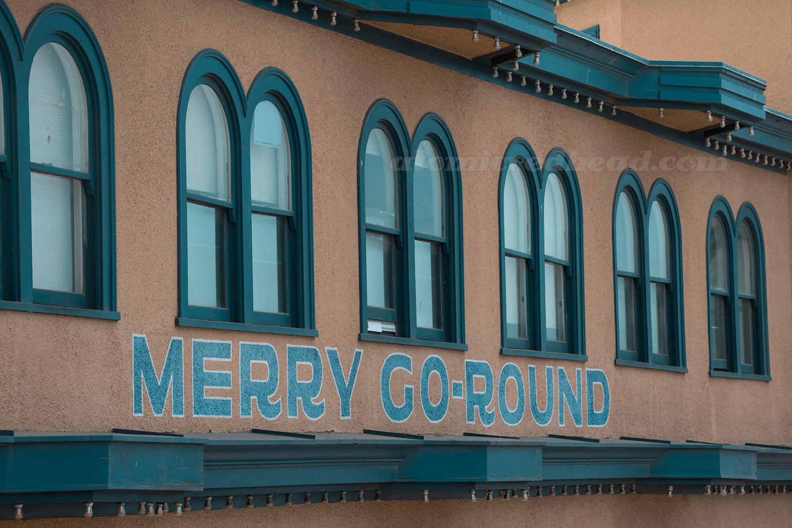 Side of the Hippodrome, a tan building, with navy blue trim, and painted on the side "Merry-Go-Round"