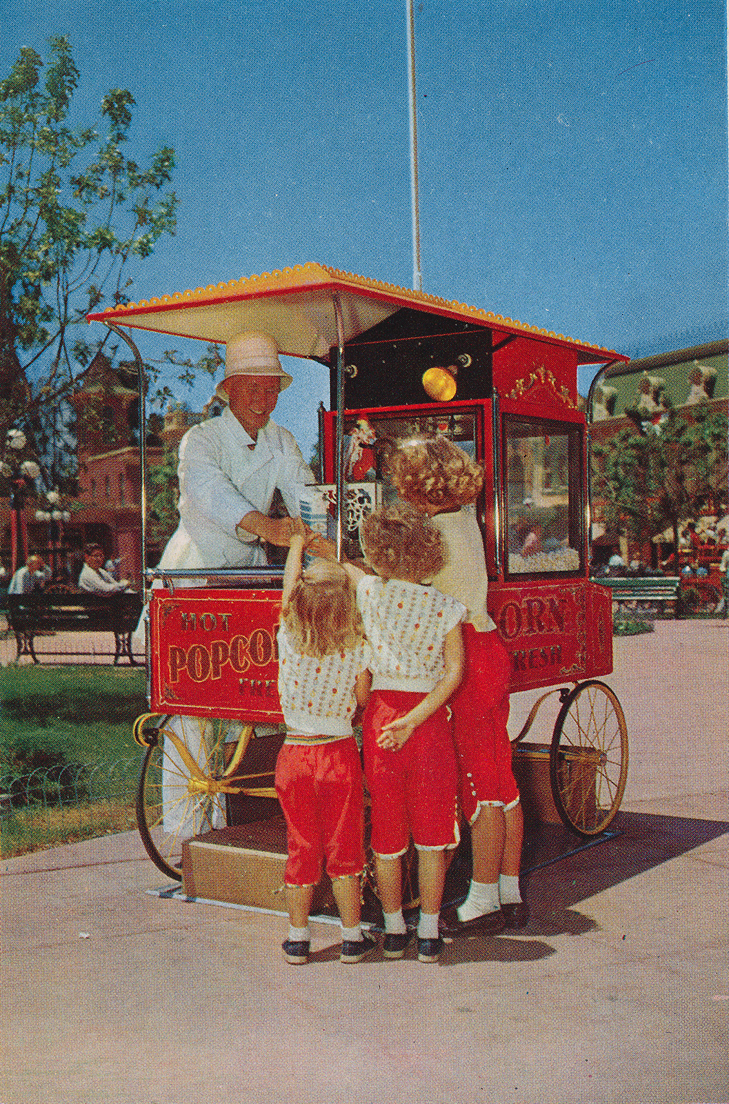 A vendor along Main Street sells popcorn to a trio of little girls all dressed alike.