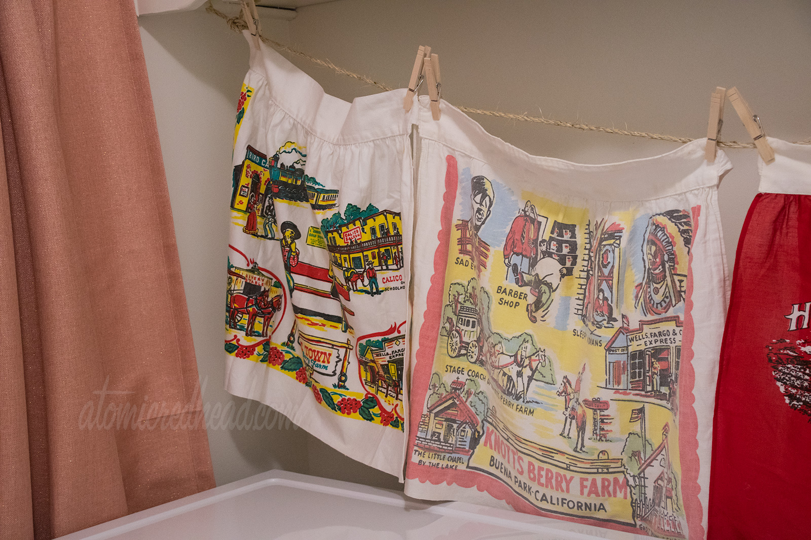 A tighter shot of the two Knott's Berry Farm aprons, each are a color scheme of red, yellow, and black. They feature icons of the park, like the stagecoach, Sad Eye Joe, the Birdcage, and the Saloon.