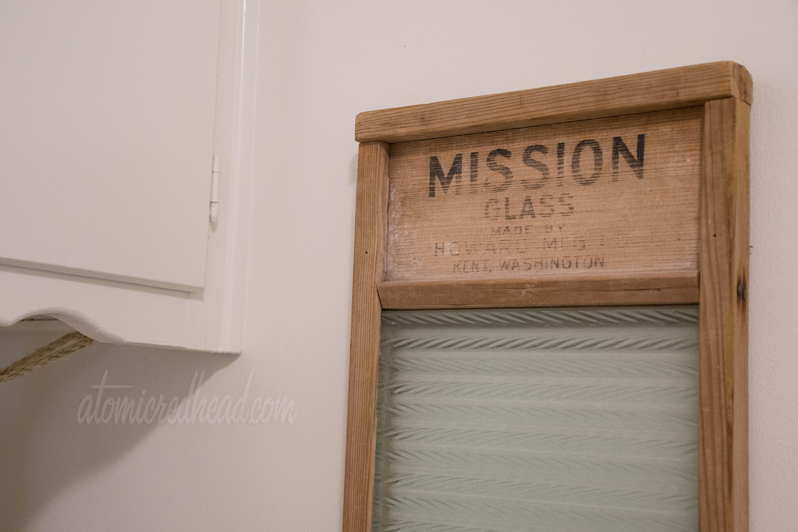 A close up of the vintage washboard, made of wood and glass, reads "Mission Glass" across the top in black letters.