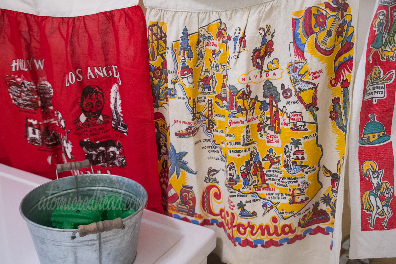 A closer look at the map of California apron, in red, yellow, and blue illustrations of various icons of the state, like the redwoods, oil wells, bears, skiers, Death Valley, and cowboys.