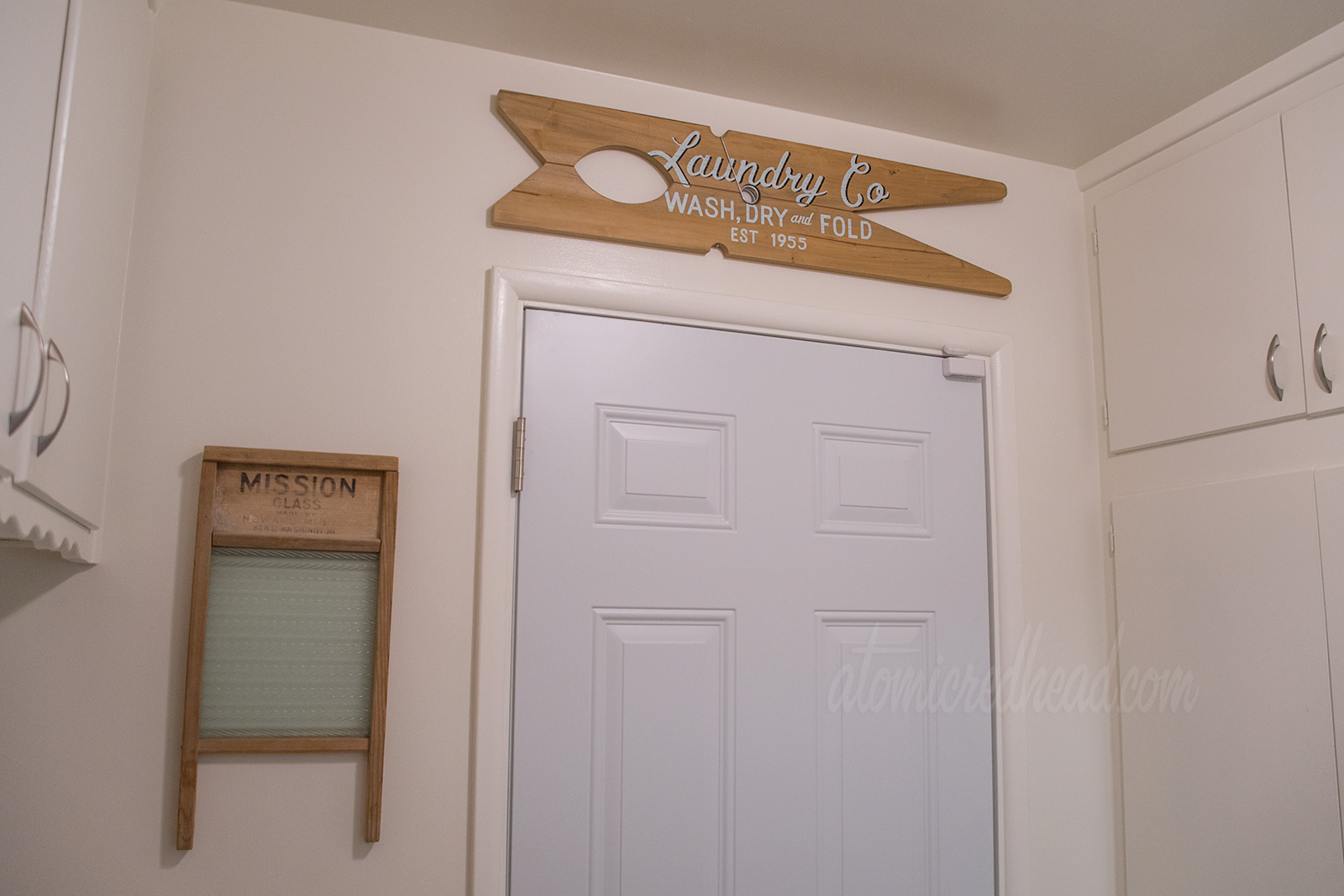 To the left a vintage washboard hangs on the wall, above the door a large clothes pin shaped sign reads "Laundry Co Wash Dry Fold Est. 1955"