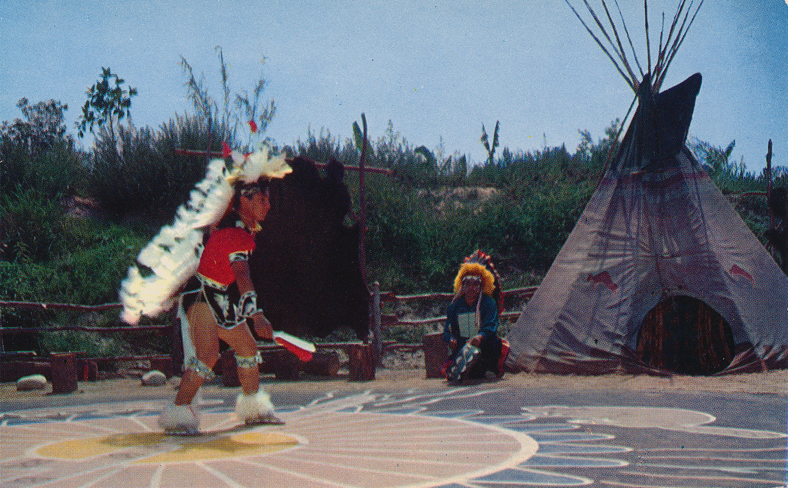 An Indian dancer with a large feather headdress dancing in the circle, a tipi sits off to the right.
