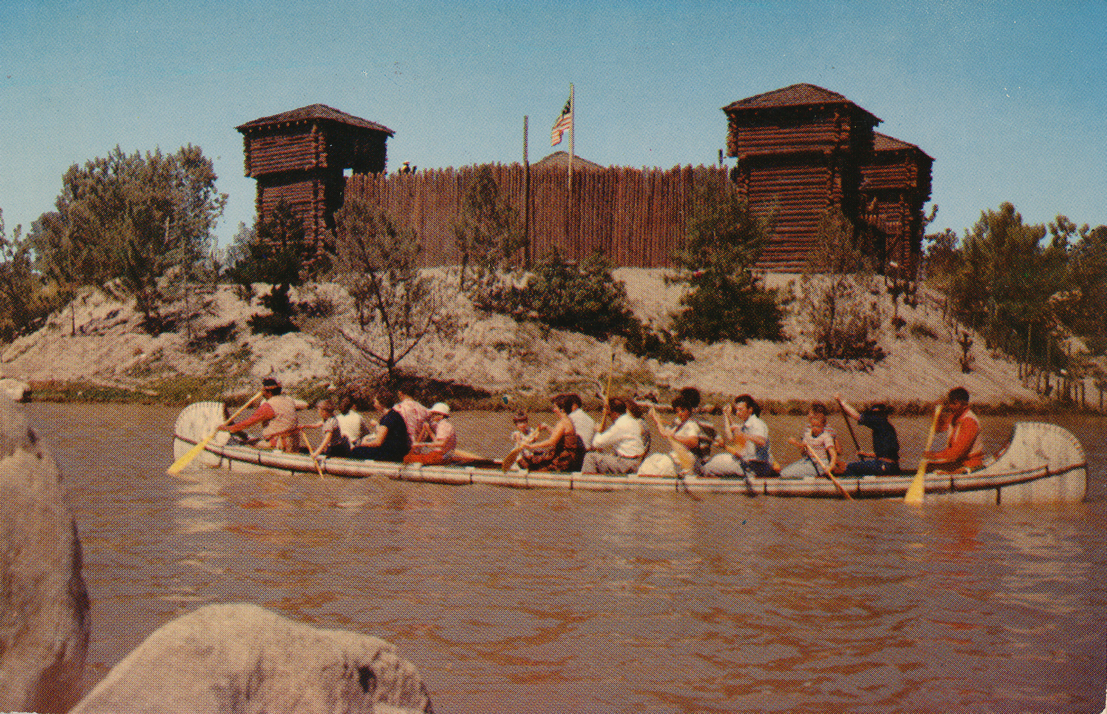 Guests paddle a canoe through the Rivers of America with Fort Wilderness in the background.