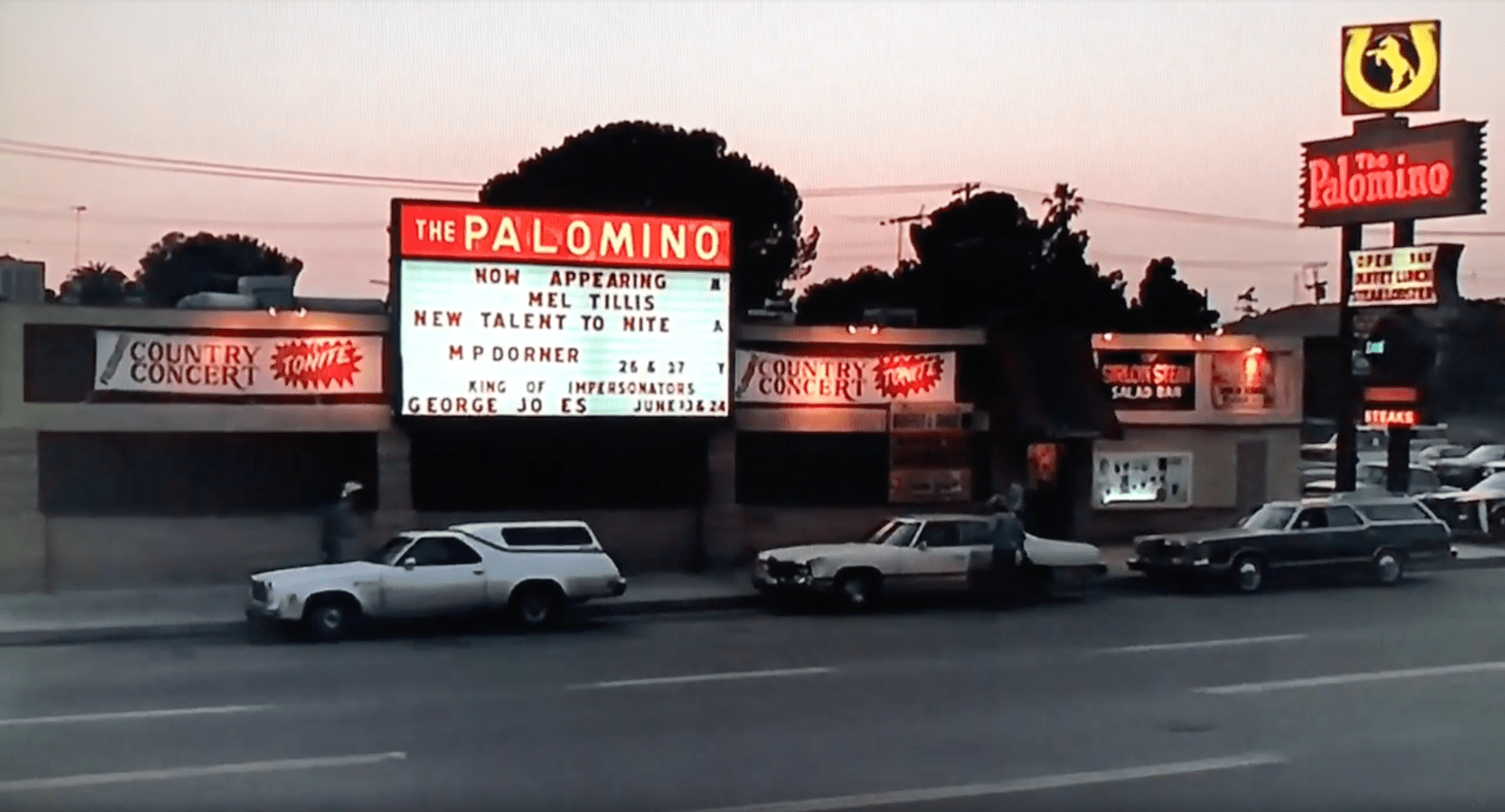 The Palomino as seen in Every Which Way But Loose, a wide but tall marque stands in the middle, with red neon reading "The Palomino" to the right a tall sign with red neon reading "The Palomino" and above it a yellow neon with a yellow horseshoe and horse in the middle of it.