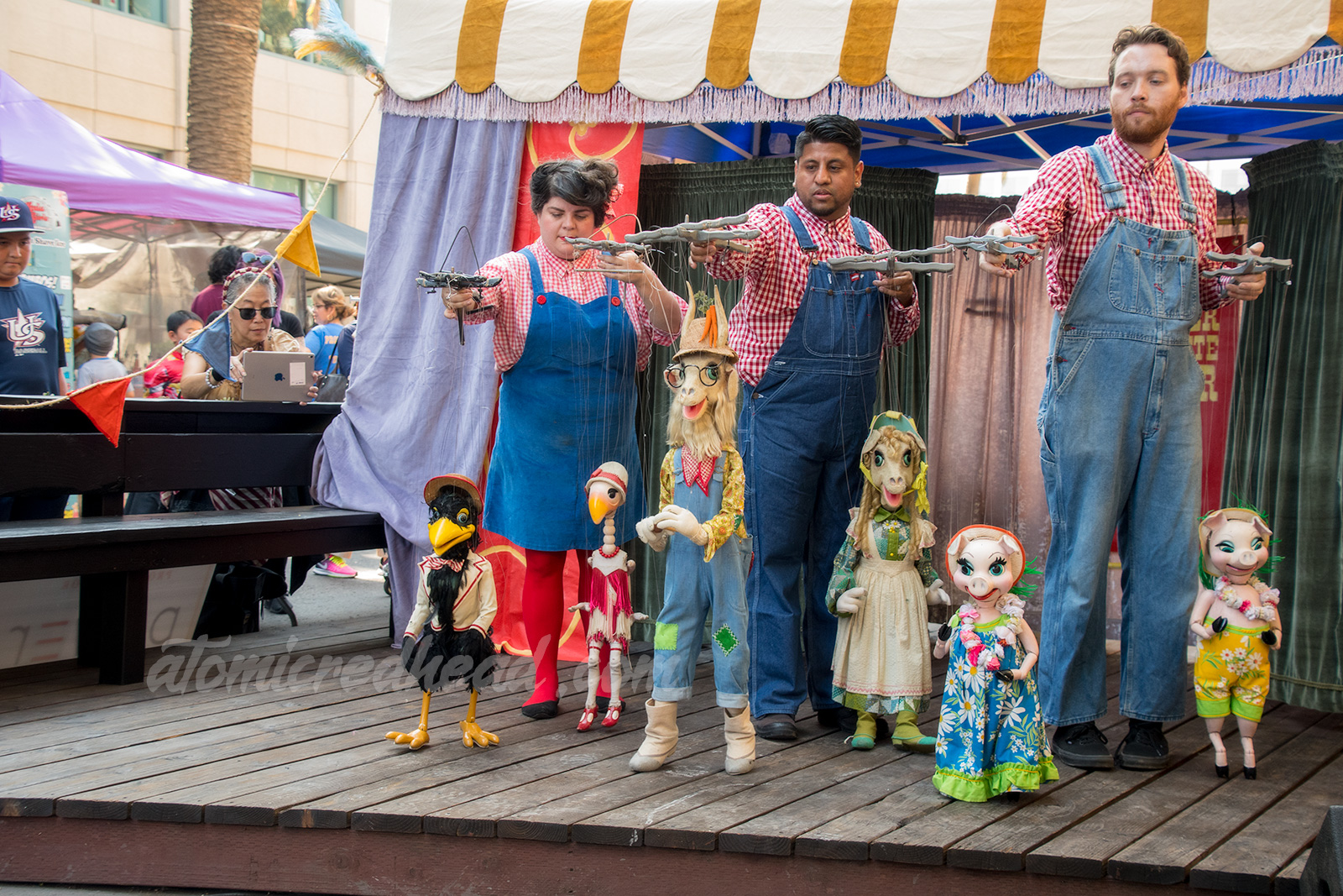The Bob Baker Marionette performers hold puppets, including a crow, goose, two goats, and two pigs, each of which are wearing clothing.