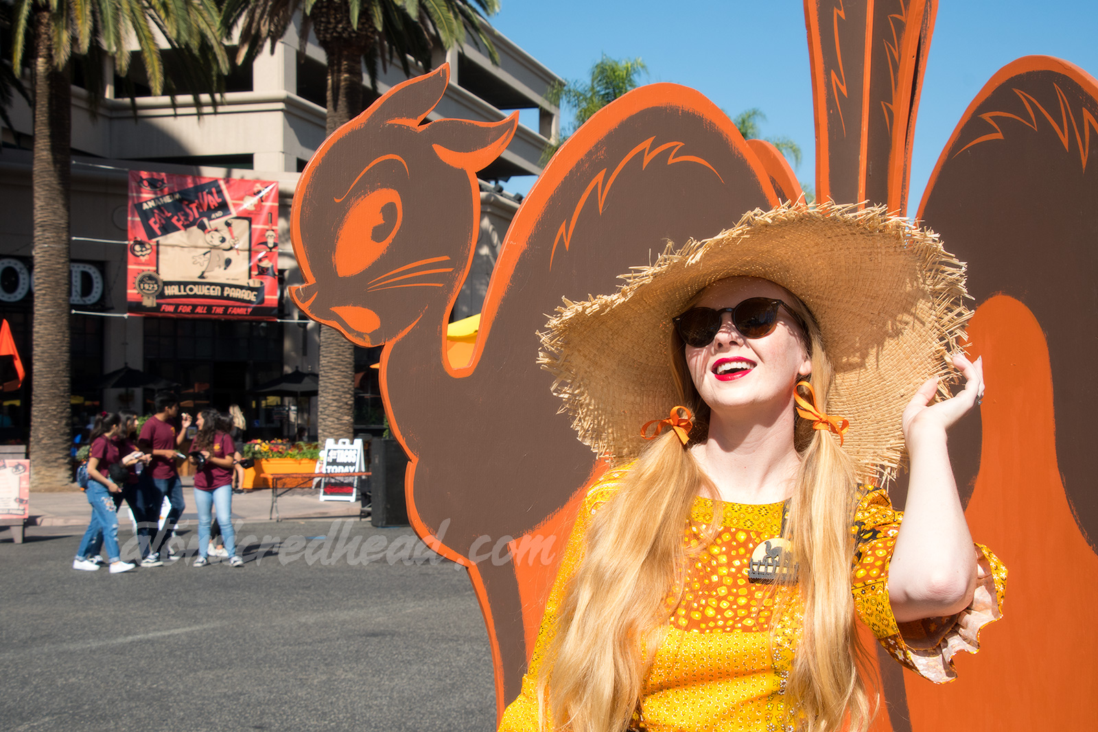 Myself standing in front of a quartette of black cats of wood, wearing a patchwork print dress of orange, yellow, black and white, as a large straw hat