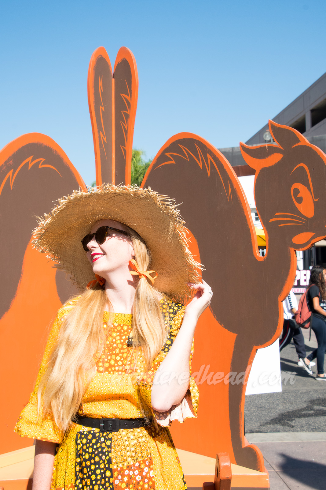 Myself standing in front of a quartette of black cats of wood, wearing a patchwork print dress of orange, yellow, black and white, as a large straw hat