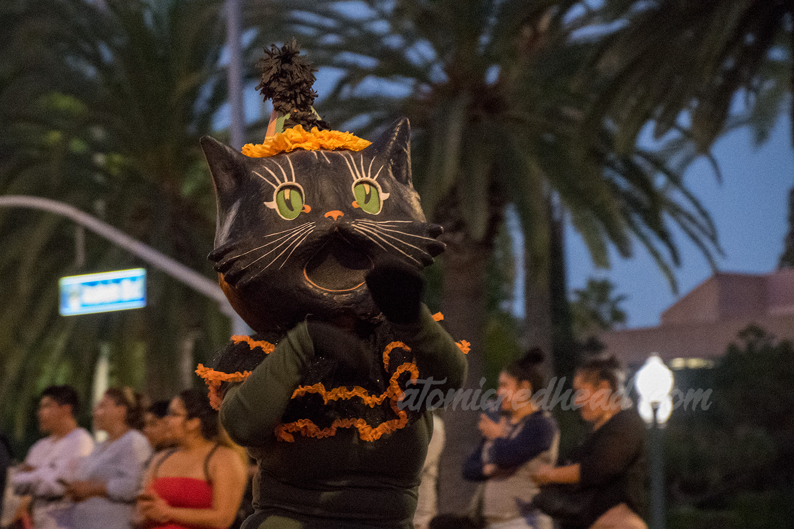 A parade performer wears a large black cat mask.