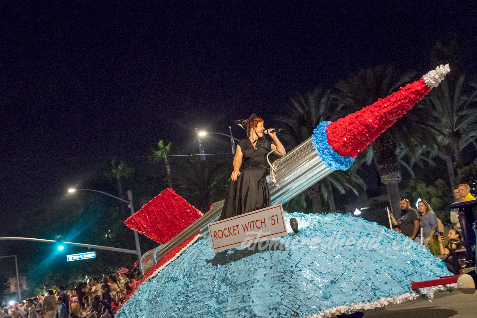 A large silver and red rocket float with the "Rocket Witch" sitting atop, wearing a black dress and black witch hat.