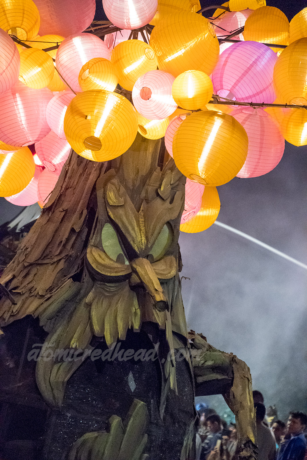 A spooky tree with a face and pink and orange lanterns hanging from its branches.