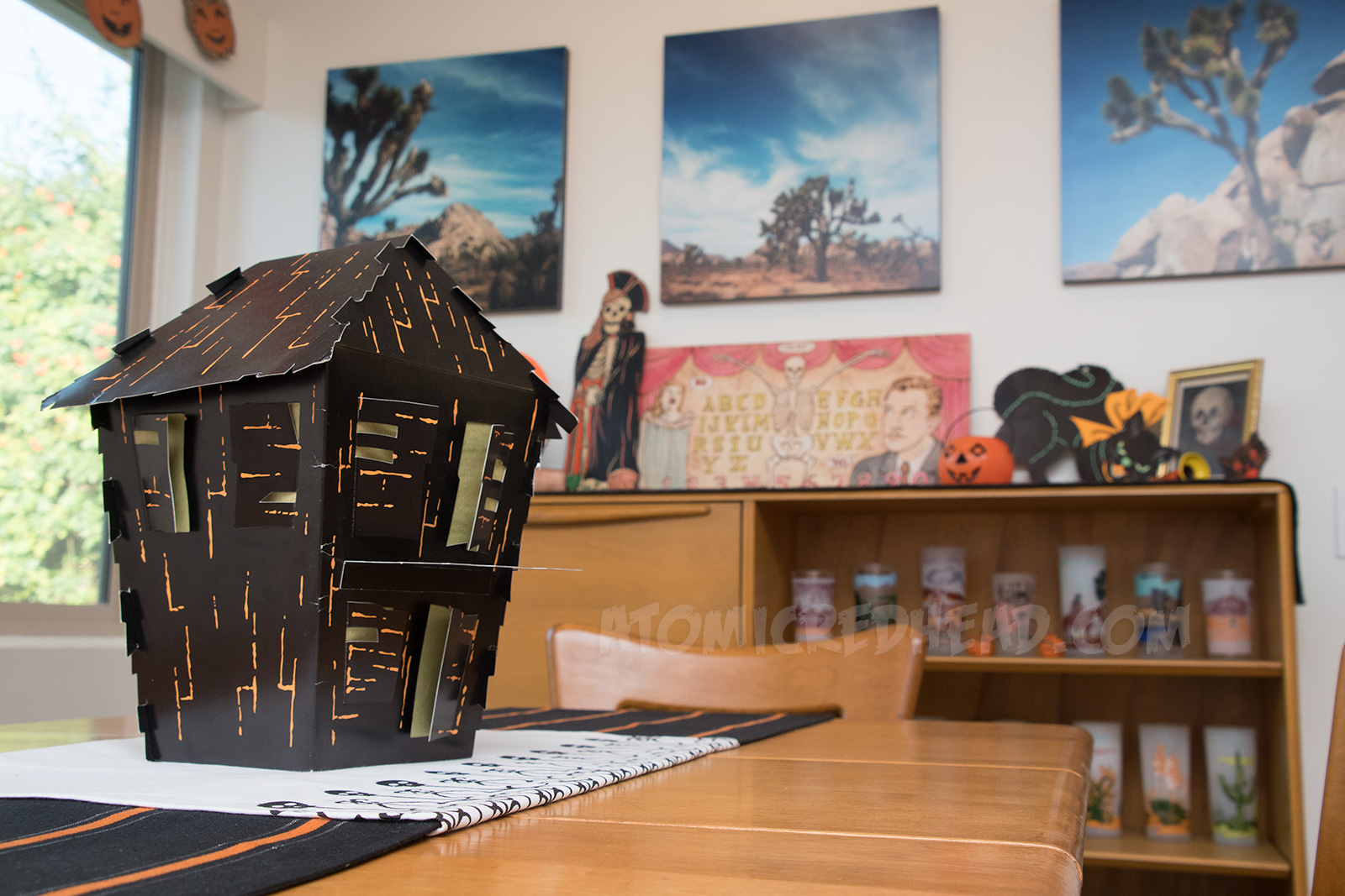 A cardboard haunted house, with shutters that are open, revealing yellow tissue paper behind them.