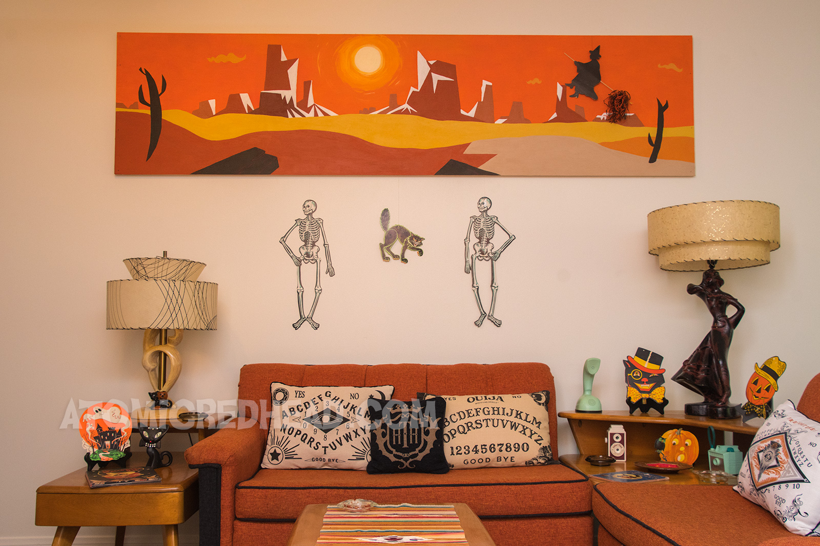 Above our couch hang two skeletons and a black cat, which have been hanged using string tied to the tops of them, and the string tapped behind the painting.