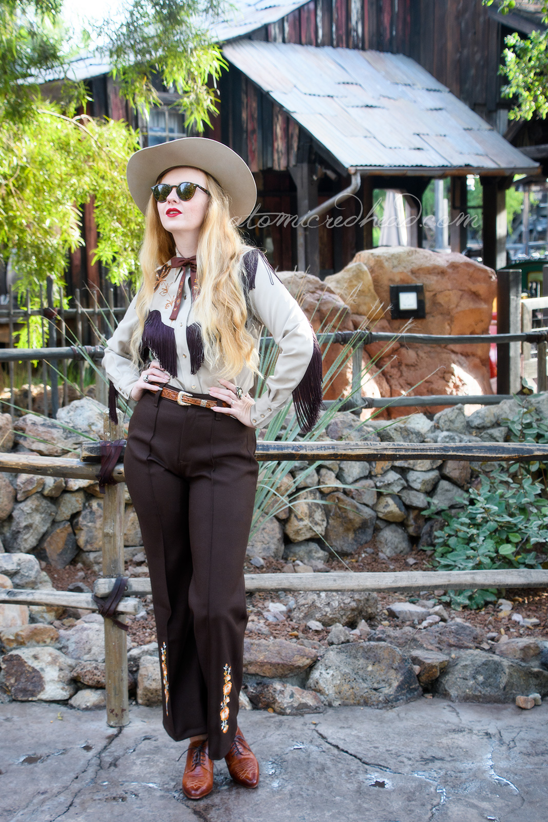 Myself, standing in front of Big Thunder Railroad, wearing a tan cowboy hat, a tan western wear shirt with dark brown fringe, and embroidered flowers, a dark brown string tie with painted flowers, and dark brown western pants with orange flowers embroidered near the bottom.