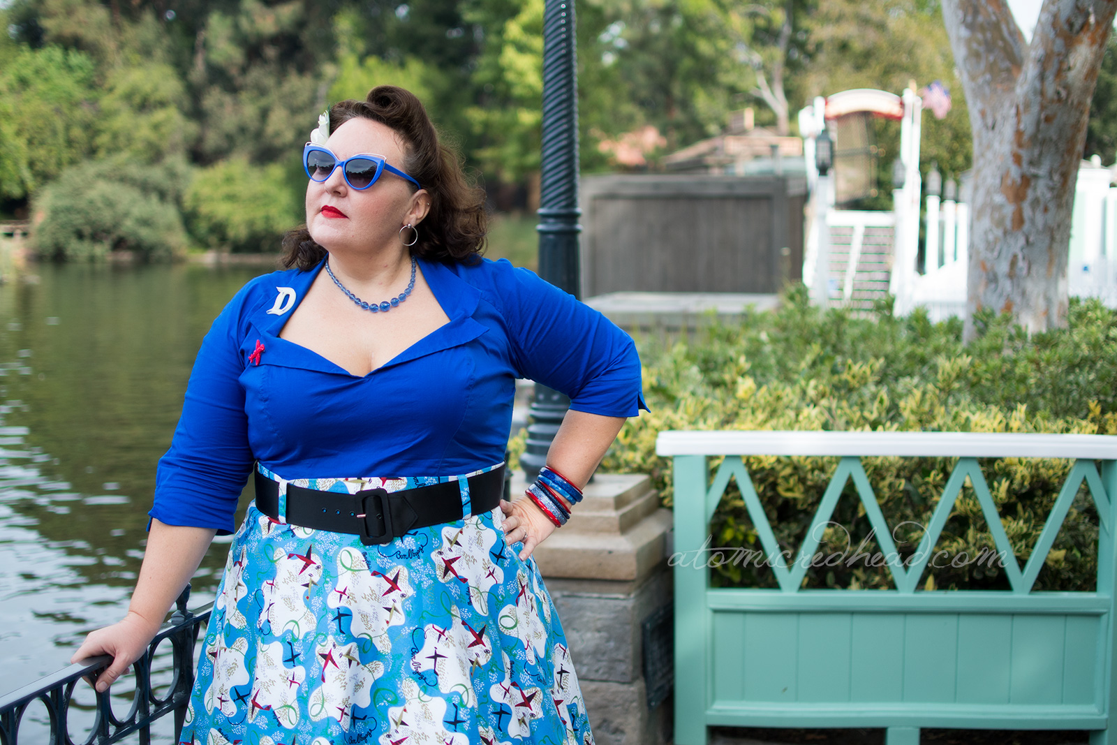 Dor stands on the banks of the Rivers of America, wearing a bright blue top, with a white D brooch, and red airplane brooch, and a skirt of blue and white with small air