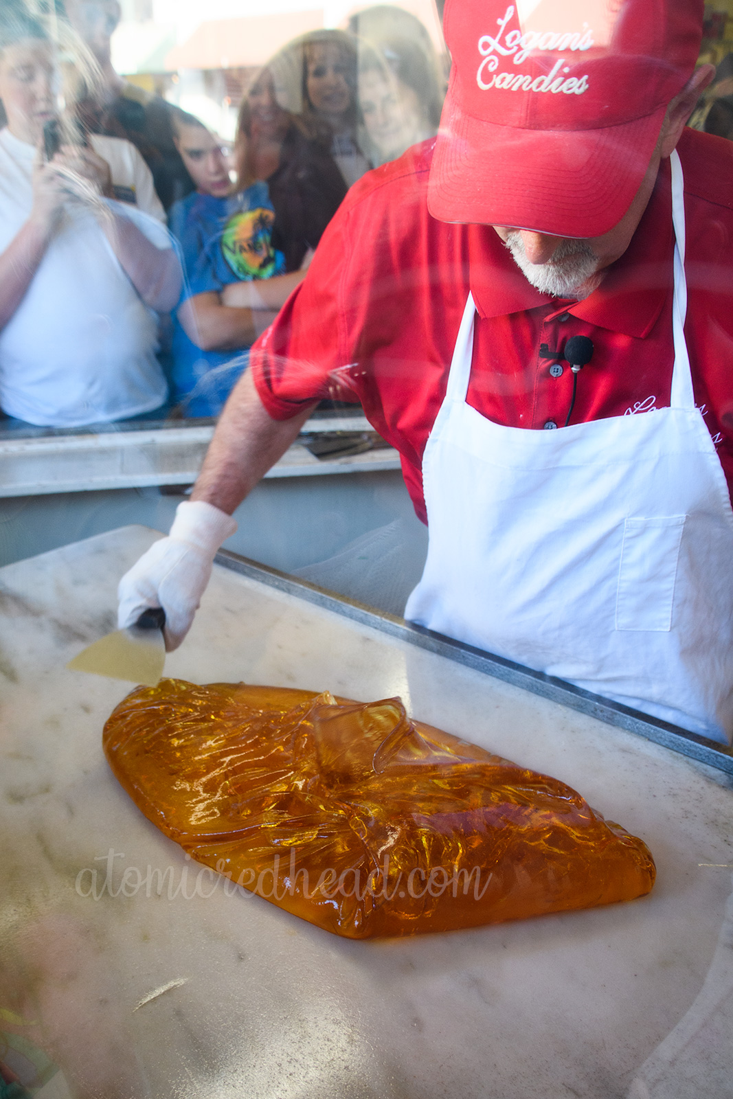 Jerry, the candy maker uses a scraper against a white marble table to work with the amber colored gooey sugar.