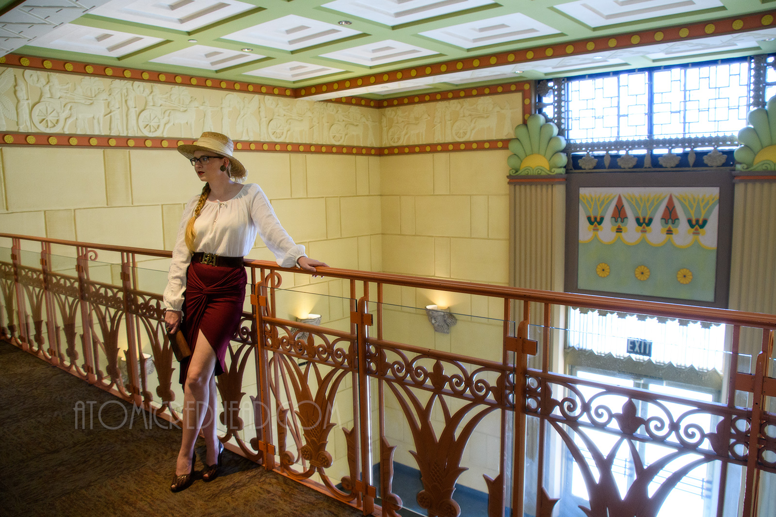 Myself standing inside, on the balcony, wearing a straw hat, a white peasant top, and maroon skirt that features gathering in an asymmetrical design.
