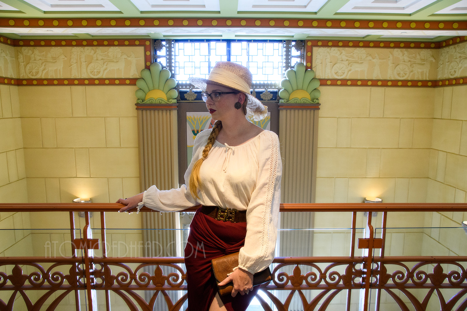 Myself standing inside, on the balcony, wearing a straw hat, a white peasant top, and maroon skirt that features gathering in an asymmetrical design.