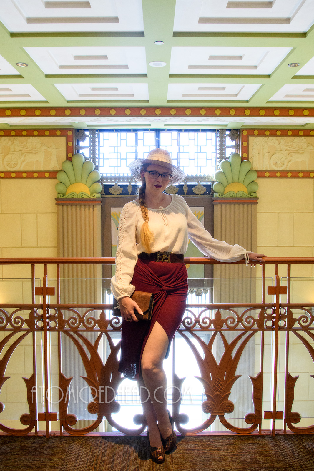 Myself standing inside, on the balcony, wearing a straw hat, a white peasant top, and maroon skirt that features gathering in an asymmetrical design.