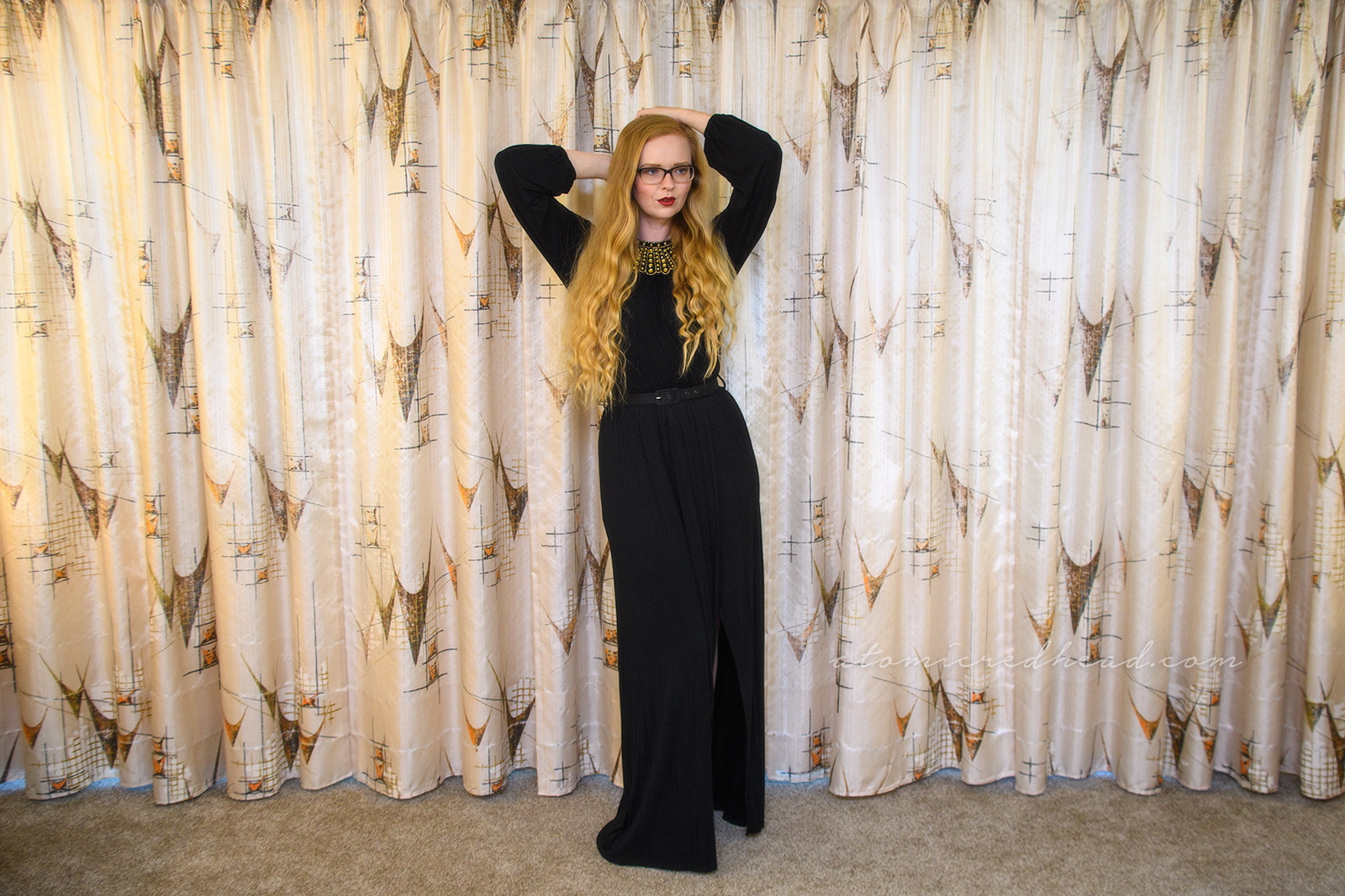 Myself wearing a long sleeve, full length black dress, with a slit up the side, wearing an art decor fan style necklace of gold rhinestones.