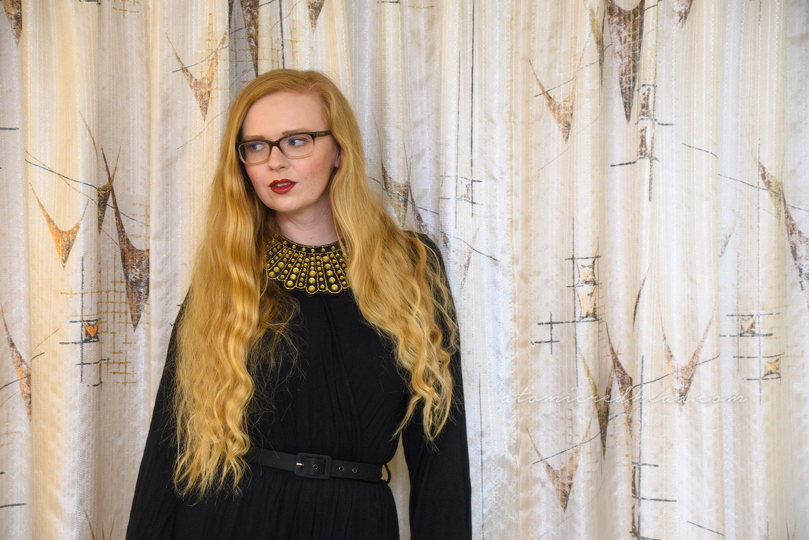 Myself wearing a long sleeve, full length black dress, with a slit up the side, wearing an art decor fan style necklace of gold rhinestones.