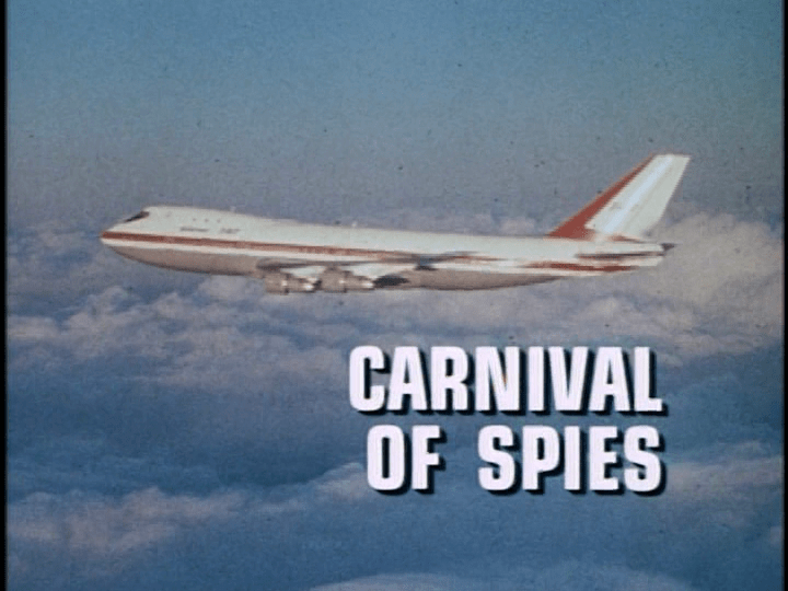 Screencap: A plane flies through a blue sky, white text reads "Carnival of Spies"
