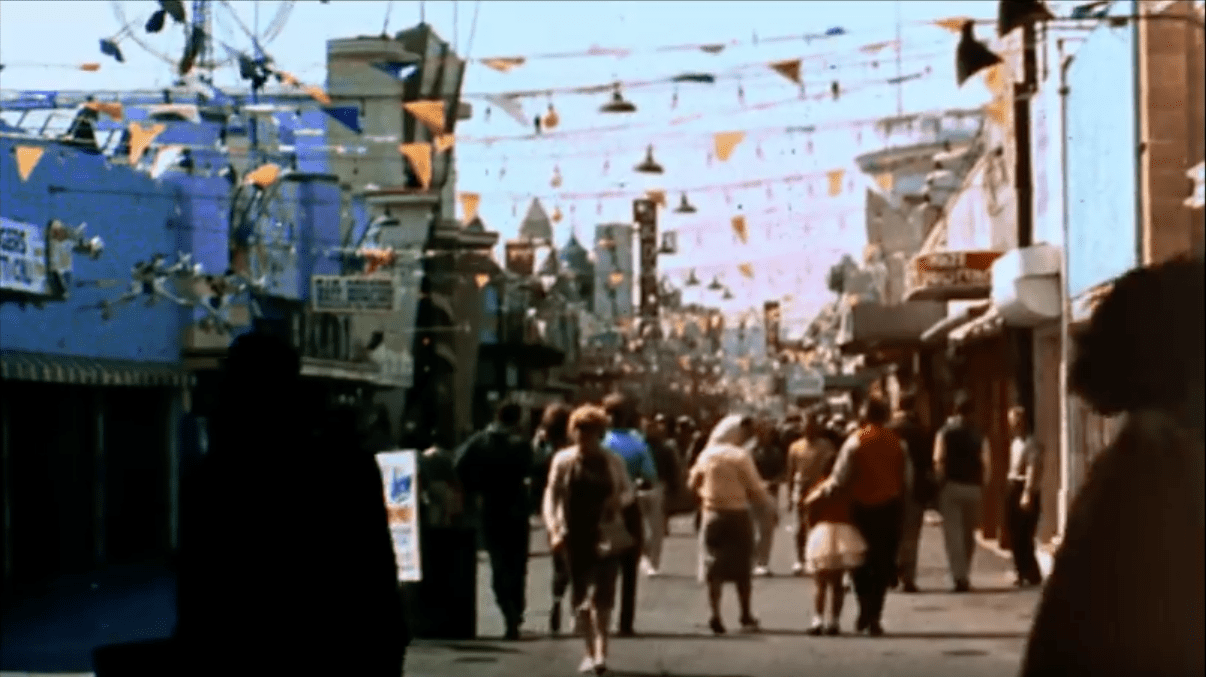 Screencap: The midway of The Pike, with flags stretched across the thoroughfare.