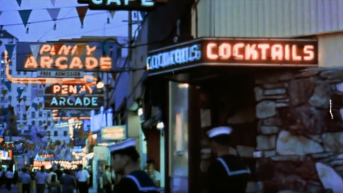 Screencap: neon for cocktails and penny arcades glow along the midway.