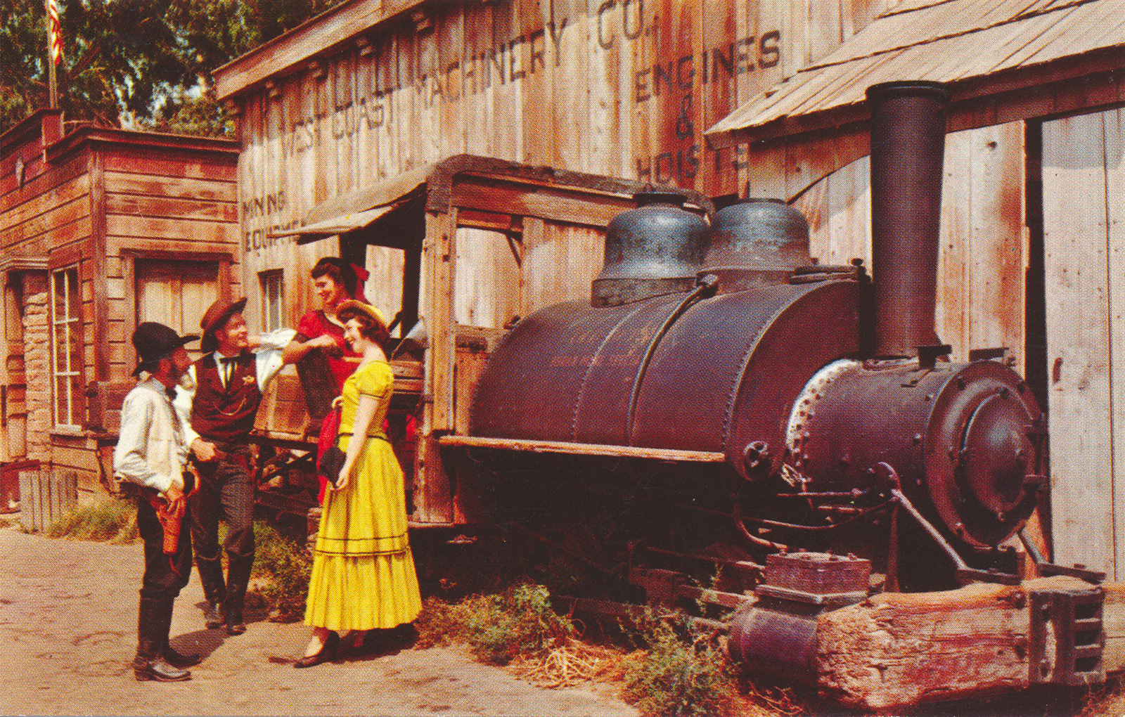 Two cowboys talk to two well dressed ladies near an old borax train.