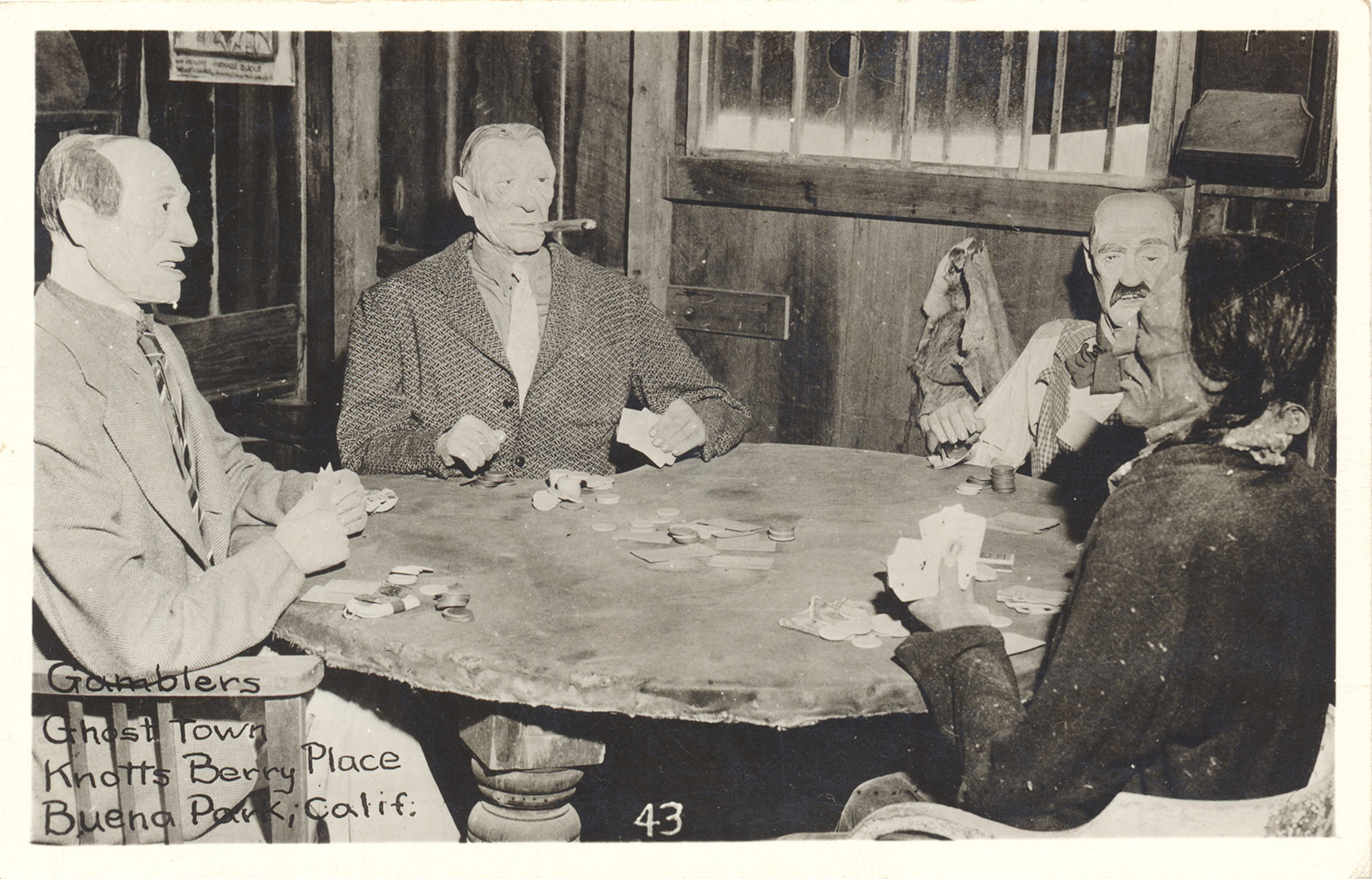 A black and white image of mannequins at a table playing cards.