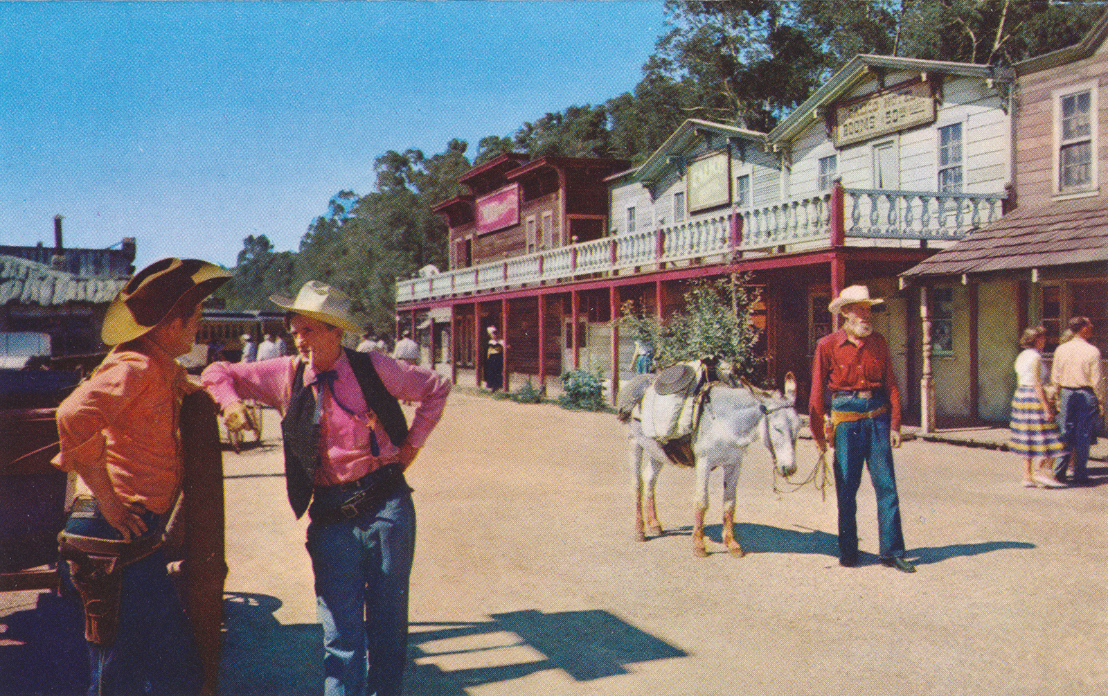 Men in old western attire stand along what is called School House Road, with old west buildings in the background.